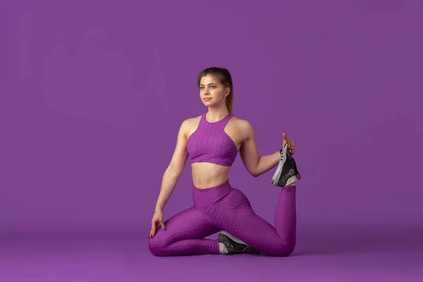 Schöne junge Sportlerin übt auf lila Studiohintergrund, monochromes Porträt — Stockfoto