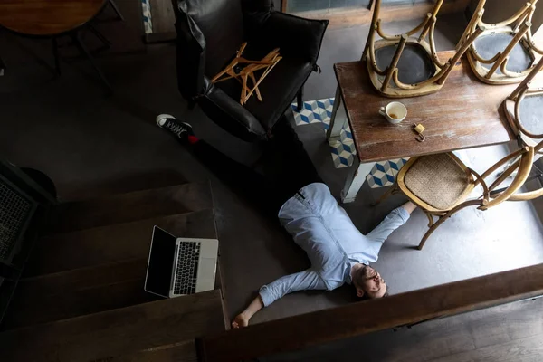 Public institutions closed due to COVID-19 or Coronavirus outbreak lockdown, stressed owner of small business alone lying down the floor in his cafe, restaurant, bar