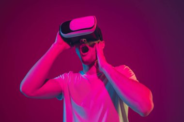 Beyaz adam portresi pembe-mor stüdyo arka planında, neon ışıkta izole edilmiş, VR-kulaklıkla oynuyor.