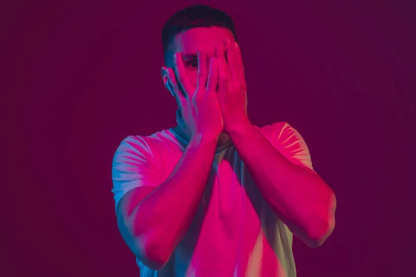 Retrato de hombre caucásico aislado sobre fondo de estudio rosa-púrpura en luz de neón, usando auriculares inalámbricos — Foto de Stock