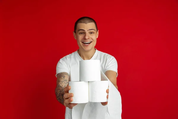 Caucasian young mans portrait on red studio background - holding toilet papers, essential goods during quarantine and self-insulation — Stock Photo, Image