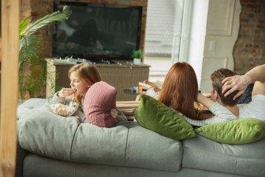 Aile evde birlikte güzel vakit geçiriyor, mutlu ve neşeli görünüyor, televizyon seyrediyor.