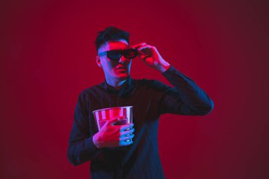 Caucasian mans portrait isolated on red studio background in purple-blue neon light, emotional and beautiful, looking throught 3D-eyewear, cinema clipart