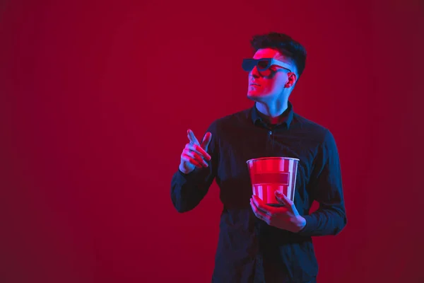 Kaukasisches Männerporträt isoliert auf rotem Studiohintergrund in lila-blauem Neonlicht, emotional und schön, Blick durch 3D-Brillen, Kino — Stockfoto