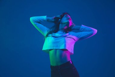 Beyaz kadın portresi mavi stüdyo arka planında izole edilmiş pembe-yeşil neon ışıklı, şık ve güzel