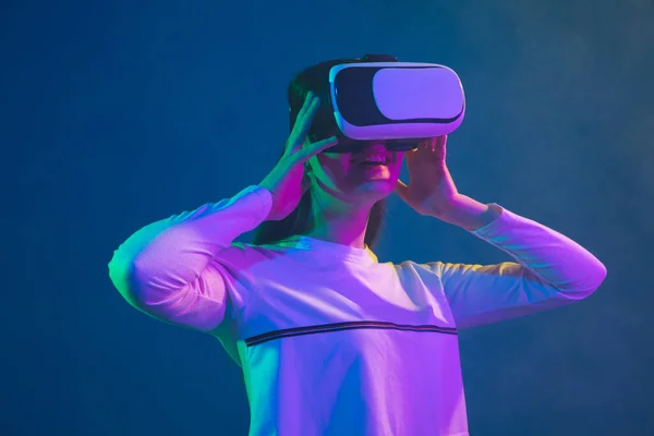 Portrait de femme caucasienne isolé sur fond studio bleu en néon rose-vert, élégant et beau, jouant avec casque VR — Photo