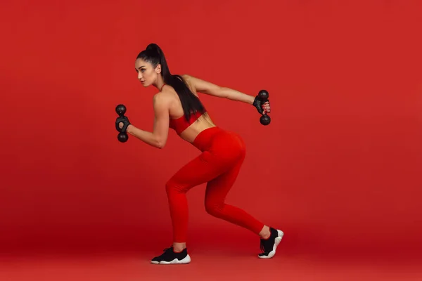 Bonita jovem atleta praticando no fundo estúdio vermelho, retrato monocromático — Fotografia de Stock