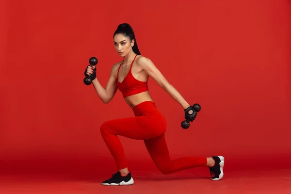 Bonita jovem atleta praticando no fundo estúdio vermelho, retrato monocromático — Fotografia de Stock