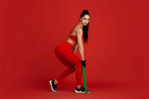 Krásná mladá žena sportovec cvičení na červeném pozadí studia, monochromatický portrét — Stock fotografie