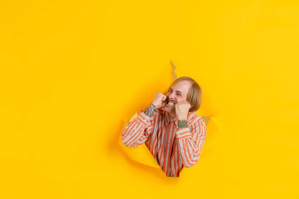 Jovem alegre posa em rasgado papel amarelo buraco fundo, emocional e expressivo — Fotografia de Stock