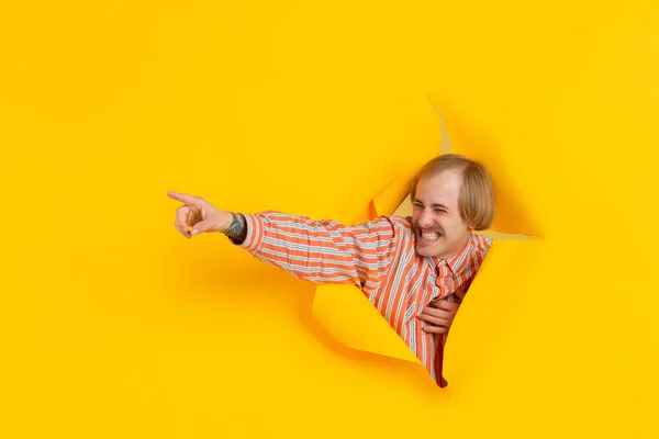 Jovem alegre posa em rasgado papel amarelo buraco fundo, emocional e expressivo — Fotografia de Stock