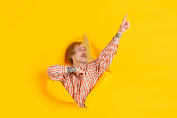 Веселий молодий чоловік позує на розірваному жовтому фоні паперової лунки, емоційно і виразно — стокове фото
