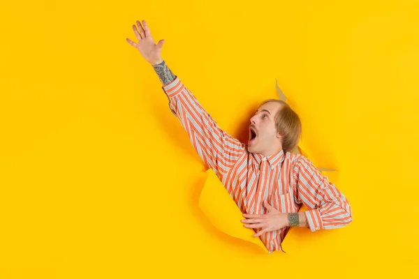 Vidám fiatalember pózol szakadt sárga papírlyuk háttér, érzelmi és kifejező — Stock Fotó