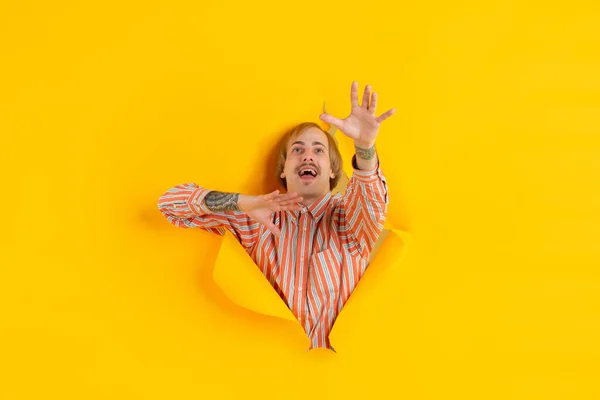 Веселий молодий чоловік позує на розірваному жовтому фоні паперової лунки, емоційно і виразно — стокове фото