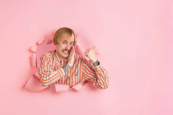 Vrolijke jongeman poseert in gescheurd koraal papieren gat achtergrond, emotioneel en expressief — Stockfoto