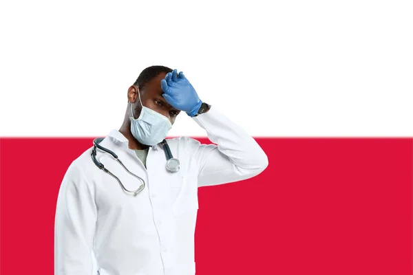 Junger Arzt mit Stethoskop und Gesichtsmaske betet für Gott mit Polens Nationalflagge im Hintergrund — Stockfoto