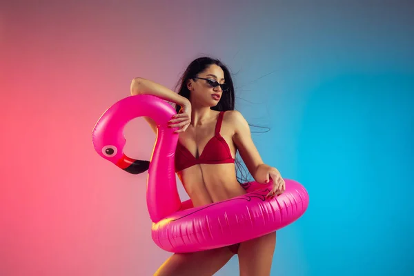 Modeporträt einer jungen, fitten und sportlichen Frau mit Gummi-Flamingo in stylischer roter Badebekleidung auf Steigungsuntergrund. Perfekter Körper bereit für den Sommer. — Stockfoto