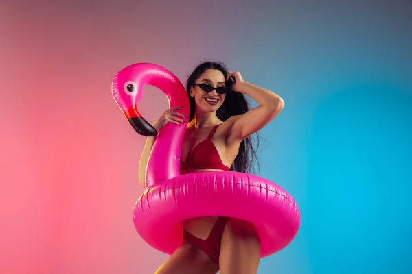 Retrato de moda de mulher jovem em forma e esportiva com flamingo de borracha em trajes de banho vermelhos elegantes em fundo gradiente. Corpo perfeito pronto para o verão . — Fotografia de Stock