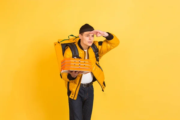 Kontaktloser Lieferservice während der Quarantäne. Der Mensch liefert während der Isolierung Lebensmittel und Einkaufstüten aus. Emotionen des Lieferanten isoliert auf gelbem Hintergrund. — Stockfoto