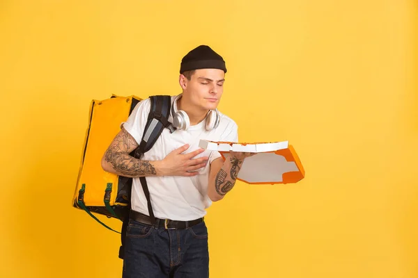 Contacless delivery service during quarantine. Man delivers food and shopping bags during insulation. Emotions of deliveryman isolated on yellow background.