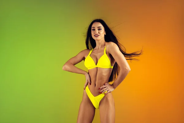 Fashion portrait of young fit and sportive woman in stylish yellow luxury swimwear on gradient background. Perfect body ready for summertime. — Stock Photo, Image