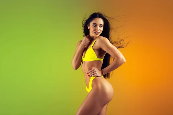 Modeporträt einer jungen, fitten und sportlichen Frau in stilvoller gelber Luxus-Badebekleidung auf Steigungsuntergrund. Perfekter Körper bereit für den Sommer. — Stockfoto