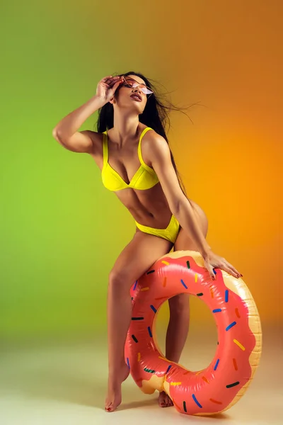 Модный портрет молодой стройной и спортивной женщины с резиновым пончиком в стильных желтых купальниках на заднем плане. Организм готов к летнему периоду . — стоковое фото