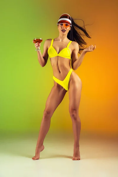 Retrato de moda de mulher jovem em forma e esportiva com coquetel em trajes de banho elegantes de luxo amarelo no fundo gradiente. Corpo perfeito pronto para o verão . — Fotografia de Stock