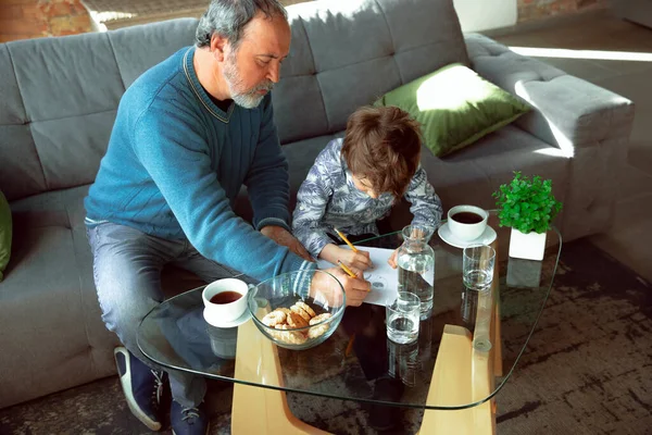 Дідусь і його онук проводять час утеплений вдома, заїкаючись, пишучи, малюючи або граючи разом — стокове фото