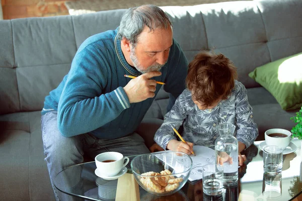 Farfar och hans sonson tillbringar tid isolerade hemma, stadfäster, skriver, tecknar eller leker tillsammans — Stockfoto