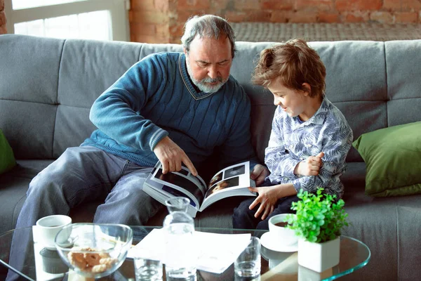 Morfar och hans barnbarn spenderar tid isolerad hemma, har roligt, läser tidningen tillsammans, glad — Stockfoto