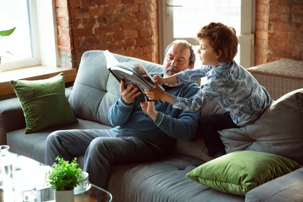 Dědeček a jeho vnuk tráví čas v izolaci doma, baví, čtení časopisu spolu, šťastný — Stock fotografie