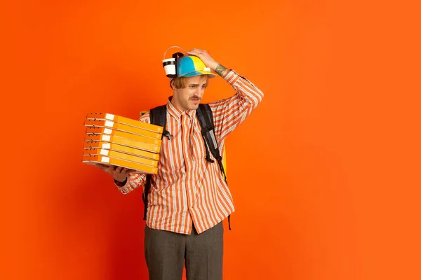 Contacless delivery service during quarantine. Man delivers food and shopping bags during insulation. Emotions of deliveryman isolated on orange background.