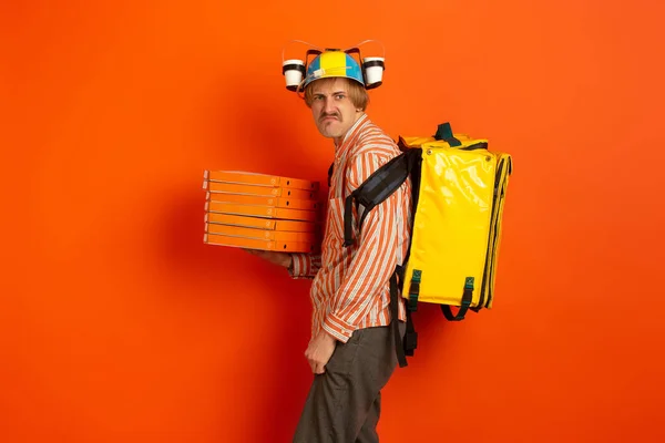 Contacless delivery service during quarantine. Man delivers food and shopping bags during insulation. Emotions of deliveryman isolated on orange background.