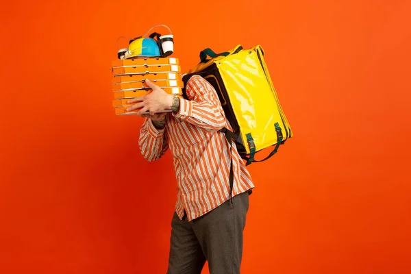 Contacless delivery service during quarantine. Man delivers food and shopping bags during insulation. Emotions of deliveryman isolated on orange background. — Stock Photo, Image