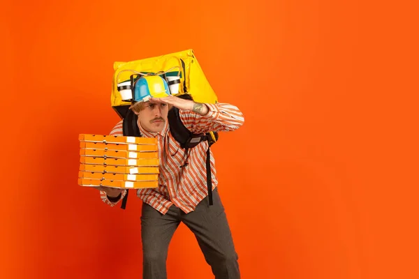 Bezdotykowa dostawa podczas kwarantanny. Człowiek dostarcza żywność i torby na zakupy podczas izolacji. Emocje doręczyciela na pomarańczowym tle. — Zdjęcie stockowe