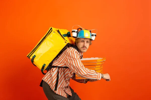 隔離中の非接触配送サービス。男は断熱材中に食品やショッピングバッグを提供します。オレンジの背景に隔離された配達員の感情. — ストック写真