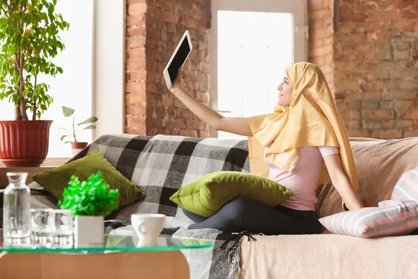 Красивая молодая мусульманка дома во время карантина и самоизоляции, с помощью планшета для селфи или видеоролика, онлайн-уроки — стоковое фото