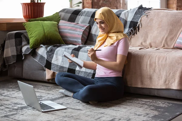 Красивая молодая мусульманка дома во время карантина и самоизоляции, с помощью ноутбука, слушать музыку, смотреть кино, сериалы, ходить по магазинам, учиться — стоковое фото