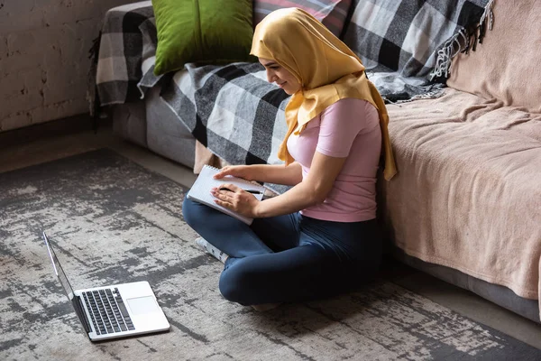 Красивая молодая мусульманка дома во время карантина и самоизоляции, с помощью ноутбука, слушать музыку, смотреть кино, сериалы, ходить по магазинам, учиться — стоковое фото