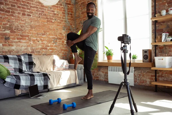 Jonge Afrikaans-Amerikaanse man die thuis les geeft in online fitnesscursussen, aerobic, sportieve levensstijl tijdens quarantaine, opnieuw opnemen op camera, streamen — Stockfoto