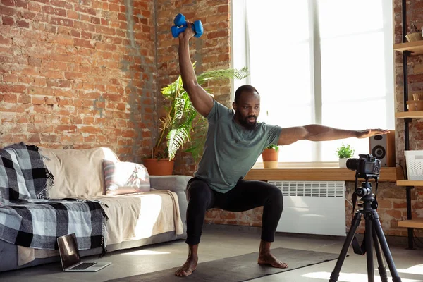 Jonge Afrikaans-Amerikaanse man die thuis les geeft in online fitnesscursussen, aerobic, sportieve levensstijl tijdens quarantaine, opnieuw opnemen op camera, streamen — Stockfoto