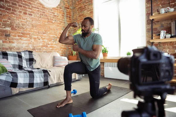 Jonge Afrikaans-Amerikaanse man die thuis les geeft in online fitnesscursussen, aerobic, sportieve levensstijl tijdens quarantaine, opnieuw opnemen op camera, streamen — Stockfoto