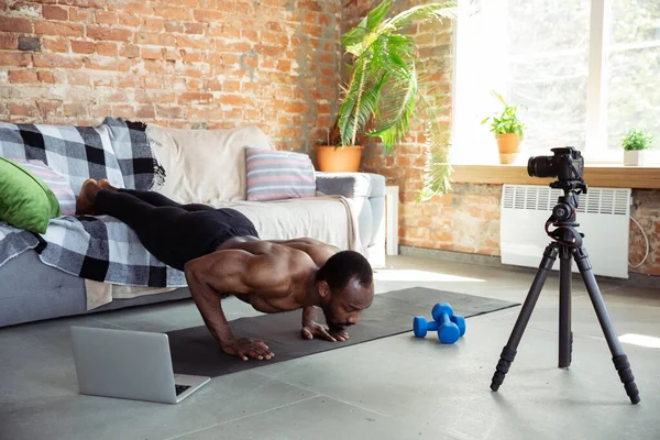 Jonge Afrikaans-Amerikaanse man die thuis les geeft in online fitnesscursussen, aerobic, sportieve levensstijl tijdens quarantaine, opnieuw opnemen op camera, streamen — Stockfoto