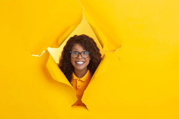 Веселая молодая женщина позирует в разорванной желтой бумажной дыре фон, эмоциональный и выразительный — стоковое фото