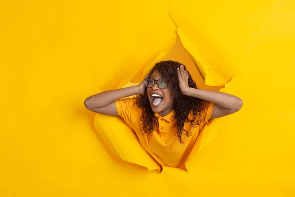 Joven alegre posa en el fondo del agujero de papel amarillo rasgado, emocional y expresivo — Foto de Stock