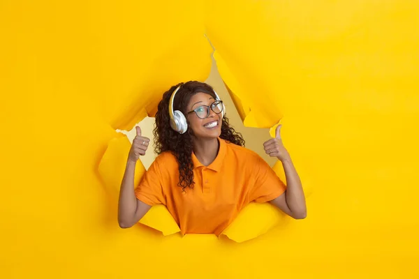 Vrolijke jonge vrouw poseert in gescheurd geel papier gat achtergrond, emotioneel en expressief — Stockfoto
