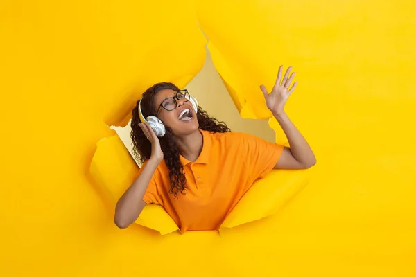 Veselá mladá žena pózuje v roztrhaných žlutých papírových dírkách pozadí, emocionální a expresivní — Stock fotografie