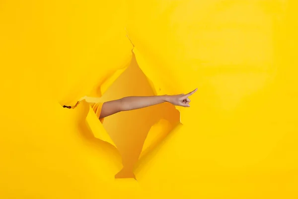 Женская рука указывая на рваные желтые бумажные отверстия задний план, празднование — стоковое фото