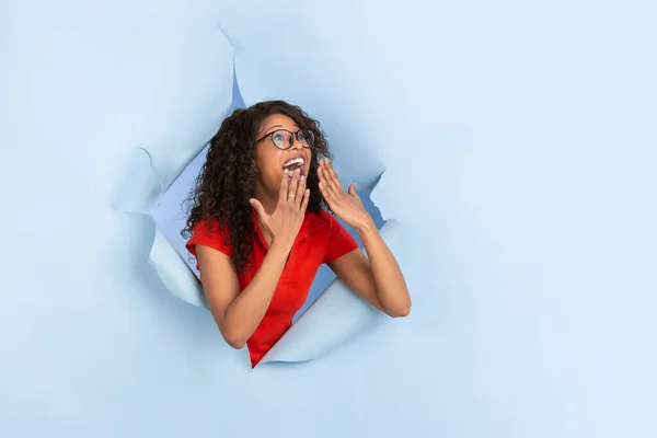 Jovem alegre posa em rasgado papel azul buraco fundo, emocional e expressivo — Fotografia de Stock